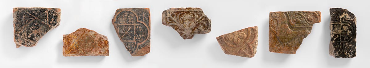 Fragments of Medieval tiles from Butley Priory, Suffolk, showing a lion rampant, the arms of Hugh Bigod, a cruciform acanthus design, fleur-de-Lis, a lion passant with floreated tail. Photo: FXP Photography, used by permission of Orford Museum.