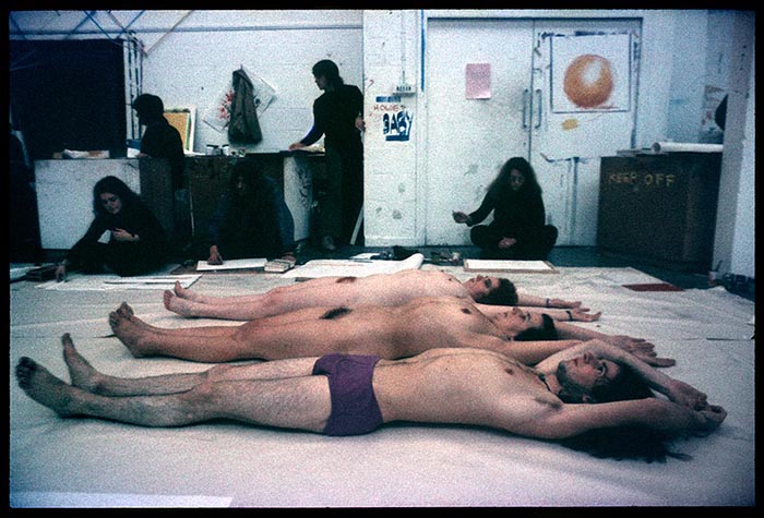 Three naked figure lying parallel to each other on white paper on an art school studio floor